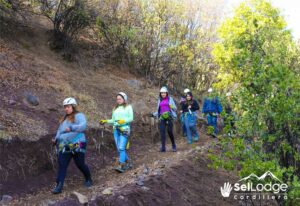 People walking down a path with helmets and gear around there waist with trees and dirt bank.