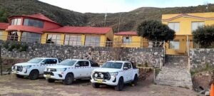 Hotel behind a large wall with trucks in front with trees and a mountains.