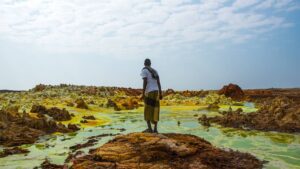 Danakil Depression – Volcanic Wonders 1 A traveler stands amid the colorful mineral deposits and volcanic terrain of Ethiopia’s Danakil Depression.