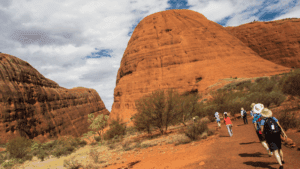 Uluru & Kata Tjuta – Australia Outback Safari Guide 4 Several hikers with backpacks walking along the base of Uluru (Ayers Rock) in Australia’s Outback on a clear day.