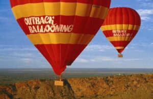 Two hot air balloons floating over the Australian Outback near Alice Springs, with vast desert landscapes stretching below.