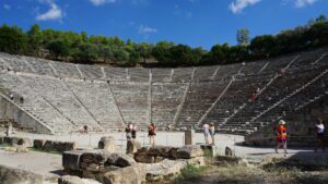 Ground-level view of an ancient amphitheatre, showing stone seating and the performance area.”