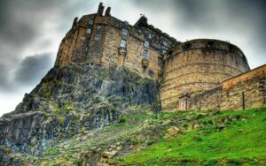 Edinburgh Castle, Scotland: A Historic Highland Fortress 3 View of Edinburgh Castle from the base of Castle Rock, with a historic statue and trees in the foreground.