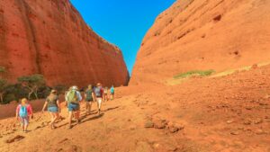 Uluru & Kata Tjuta – Australia Outback Safari Guide 3 Several hikers with backpacks walking along the base of Uluru (Ayers Rock) in Australia’s Outback on a clear day.