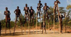 Members of an Omo Valley tribe walking on stilts over open terrain, showcasing traditional practices and unique cultural expressions.