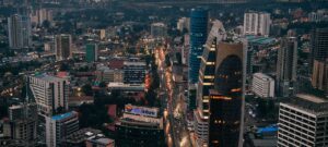 City with buildings and streets and cars on the roads lit up buildings and lights on cars.