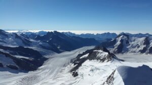 Hiker walking along the Aletsch Glacier trail in Switzerland, with the massive glacier stretching below and alpine peaks in the background.