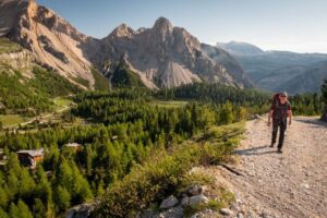 Person walking on a mountain trail with trees covering the valley below.