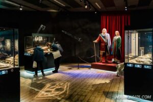 Two visitors observing exhibits inside the Lofotr Viking Museum in Lofoten, Norway.