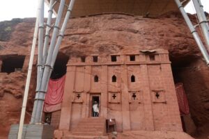 A rock-hewn church in Lalibela, Ethiopia, carved below ground level into volcanic stone with an entrance and surrounding trenches.