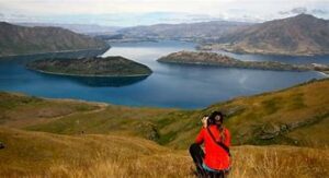 Woman sitting on a hill overlooking a canyon with a lake and steep mountain cliffs in New Zealand.