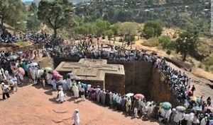 A large group of people standing on a cliff or elevated viewpoint, overlooking Lalibela’s rock-hewn churches and surrounding landscape in Ethiopia.”