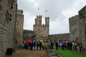 Caernarfon Castle, Wales: A Majestic Medieval Fortress 3 Group of people holding umbrellas while observing Caernarfon Castle in North Wales.