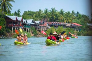 Mekong River Expeditions – Exploring Laos’ Majestic Waterway 3 Groups of people kayaking in several boats along a scenic river surrounded by nature.