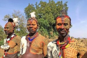 Three members of a local Omo Valley community stand near a cliff, overlooking the dramatic landscapes of southern Ethiopia