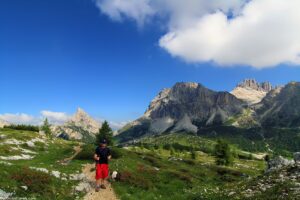 Person walking on a mountain trail carrying a backpack, surrounded by rugged peaks.