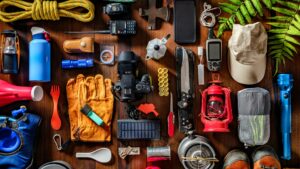 Camping supplies and outdoor gear setup featuring tents, backpacks, lanterns, cooking equipment, sleeping gear, and adventure essentials in a scenic wilderness setting.
