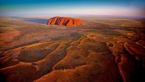 Uluru & Kata Tjuta – Australia Outback Safari Guide 2 Aerial view of Uluru (Ayers Rock) rising from the red desert landscape in Australia’s Outback, seen from a distance.