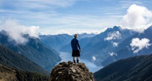 Person standing on a ledge overlooking a valley with steep slopes and a lake in New Zealand.