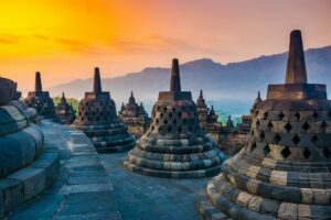 🌄 Explore Borobudur, Indonesia: Majestic Temples, Sunrise Views & Cultural Adventures 1 Acorn-shaped stupas atop Borobudur Temple in Indonesia, with distant temples and a mountain backdrop.