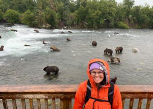 Woman standing on a balcony overlooking a river with several bears below.”