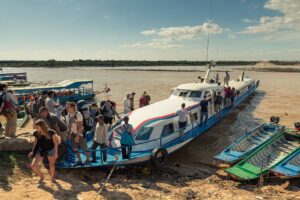 Tourists disembarking from a long tour boat onto a riverbank or shore.