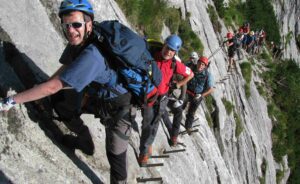 Hikers walking along iron spikes and cliff-side trails on the Zugspitze, carrying backpacks, with panoramic alpine views in Germany and Austria.