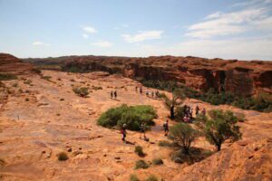 Several people walking along the rim of a canyon, with steep cliffs and expansive natural scenery in the background.