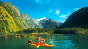 Several people canoeing on a lake with forested mountains in the background in New Zealand.