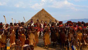 Local community members in Ethiopia’s Omo Valley gathered outdoors, talking and socializing near traditional huts and open fields.
