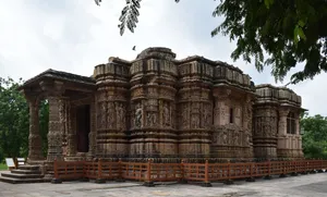 Historic stone temple in India featuring intricately carved pillars, sculpted figures, decorative walls, and traditional architecture surrounded by green trees.
