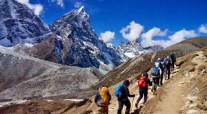 Group of hikers with backpacks walking along a mountain trail surrounded by peaks and valleys.