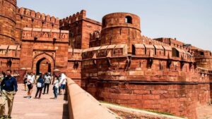 Several people entering an ancient Indian fort, walking across a historic stone bridge