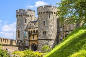 Medieval castle in England with stone walls and towers, surrounded by lush greenery.