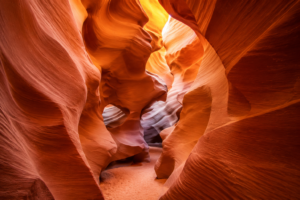 Sunlight illuminating the smooth, sculpted sandstone walls of Antelope Canyon, highlighting narrow passageways and rich orange-red hues with natural curves and textures.