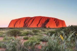 Uluru in Australia, a tall sandstone rock formation surrounded by flat desert lands.