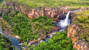 Waterfalls cascading down steep cliffs into a forested creek below.