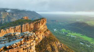 Steep cliff walls rising above a lush green valley filled with trees and vegetation.
