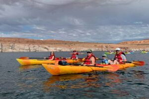 🌊 Lake Powell (Page, Arizona) Waterfront RV Camping 4 Several people in five canoes paddling across a calm lake with surrounding cliffs and mountains in the background.