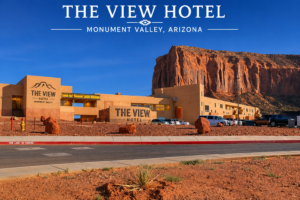 Monument Valley: Iconic Red Rock Landscape of The American Southwest 4 The View Hotel in Monument Valley, Arizona, with the iconic red sandstone cliffs rising behind the hotel under a clear blue sky.