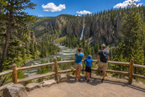 Tower Fall – Yellowstone’s Classic Waterfall 3 Family enjoying a summer overlook with views of Tower Fall, rugged canyon cliffs, evergreen forests, and river scenery in Yellowstone National Park.
