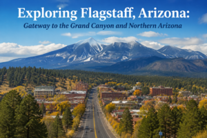 A scenic view of Flagstaff, Arizona from above showing the town nestled among pine forests with snow-dusted mountain peaks in the background under a bright blue sky.