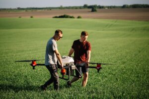 Two people carrying a large white drone with red markings below the propellers.