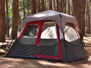 🌞🏕️⛺🎒 The Ultimate Camping & Adventure Gear Guide: 30 Tents and 20 Must-Have Outdoor Essentials 🎣🔥🍳 3 A gray and white camping tent with a red stripe set up in a peaceful forest surrounded by trees and sunlight filtering through the canopy.