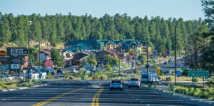 A paved road leading into a small town, surrounded by forest, with cars traveling along the road.