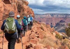Exploring Flagstaff, Arizona: Gateway to the Grand Canyon and Northern Northern Arizona 2 Five hikers with backpacks walk along a mountain trail overlooking a deep green valley, surrounded by sunlight and open sky — capturing the spirit of outdoor adventure.
