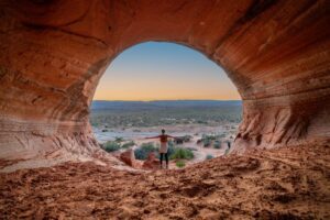 🌊 Lake Powell (Page, Arizona) Waterfront RV Camping 5 Person standing inside a cave with a large opening, looking out at cliffs, valley, or landscape beyond under natural light.