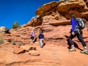 Three people walking along a scenic desert trail, one carrying a backpack.
