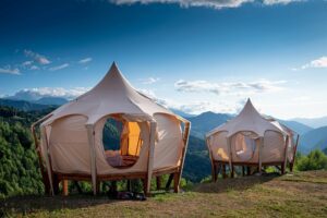 Two glamping huts on elevated platforms nestled among trees on a mountainside, overlooking scenic valleys — perfect for luxury outdoor adventures