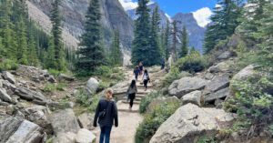 Hikers on the Moraine Lake shoreline trail with turquoise waters and snow-capped peaks in Banff National Park